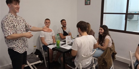 Powiększ grafikę: spotkanie w siedzibie Mobility Projects, rozgrzewka językowa, prezentuje Jakub, wokół stolika od lewej: Maciej, Paris, Agata, Małgosia, Dobromir
